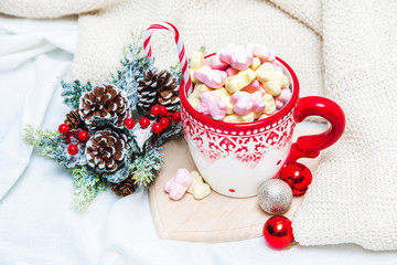 Obraz na płótnie Canvas Red mug with marshmallows and winter ornaments on a white sheets
