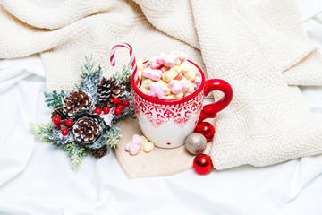 Red mug with marshmallows and winter ornaments on a white sheets