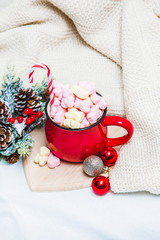Red mug with marshmallows and winter ornaments on a white sheets