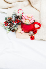 Fototapeta na wymiar Red mug with marshmallows and winter ornaments on a white sheets