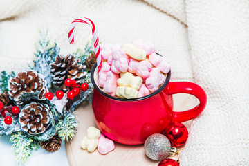 Red mug with marshmallows and winter ornaments on a white sheets