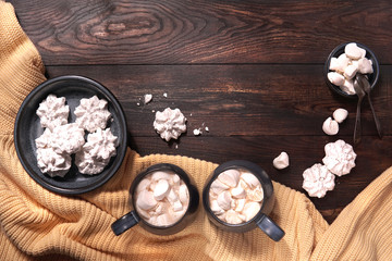Two blue mugs of hot drink with marshmallow on wooden table with sweet white meringues and yellow blanket. Winter, christmas dessert. Top view, flat lay, copy space.       