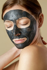 Charcoal face mask or black clay mud. Beautiful woman with black mask on her face, close up studio head shot. Natural cosmetic concept.