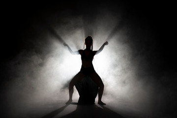 Silhouette dancer woman performing dance figures in fog.