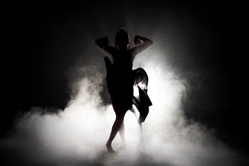 Silhouette dancer woman performing dance figures in fog.