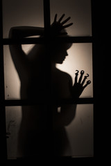 strange silhouette of a female hand with date on fingers pressed to glass of door with backlight,...