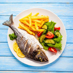 Roast fish with french fries and vegetable on wooden background