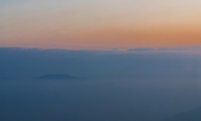 Fototapeta na wymiar Blue mountains covered with solid fog against a bright sunrise