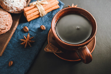 Brown cup with black coffee, cookies, cinnamon sticks, star anise on dark background