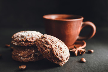Chocolate cookies with powdered sugar and brown cup with hot drink, coffee or tea on dark background