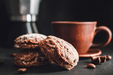Chocolate cookies with powdered sugar and brown cup with hot drink, coffee or tea on dark background