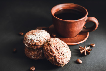 Chocolate cookies with powdered sugar and brown cup with hot coffee on dark background