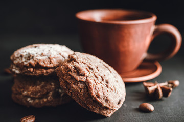 Chocolate cookies with powdered sugar and brown cup with hot drink, coffee or tea on dark background