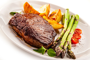 Barbecued beef steak with asparagus and fried potatoes on white background