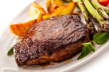 Barbecued beef steak with asparagus and fried potatoes on white background