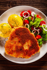 Schnitzel with boiled potatoes on timber background