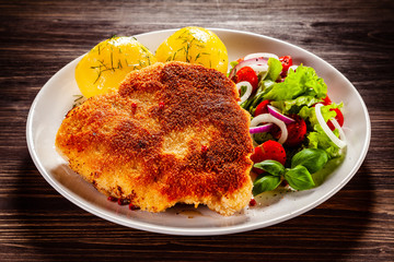Schnitzel with boiled potatoes on timber background