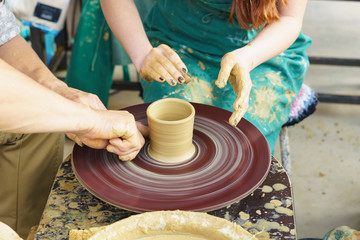 the Hands of a master and a student make a pitcher on a Potters wheel of yellow clay