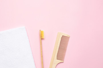 Eco wooden toothbrush , comb and white bath towel on pink background with copyspace , bathroom and spa accessory