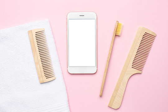 Mobile phone and eco wooden toothbrush , comb , brush for dry massage on pink background . Spa and bathroom accessories