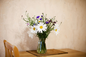 Fototapeta na wymiar daisies and cornflowers in vase on table.