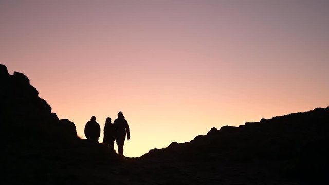 Silhouettes of a hikers walking or climbing together in a group up the mountain or a hill at sunset. Journey and destination to the top.