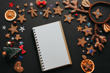 Christmas flat lay of gingerbreads decorations and an open copybook on the black background. Christmas concept. Wish list with decorations. 