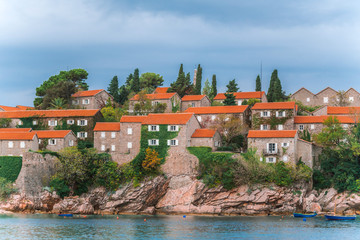 Fototapeta na wymiar Sveti Stefan island in Montenegro. Small boats are moored off the island. Mediterranean fortress. Houses with red roofs, the ancient wall of the fortress.