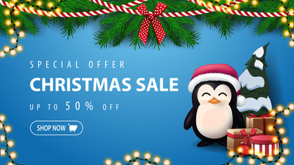 Special offer, Christmas sale, up to 50% off, blue discount banner with wreath of Christmas tree branches and penguin in Santa Claus hat with presents near the wall