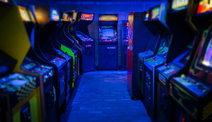 Old Vintage Arcade Video Games in an empty dark gaming room with blue light with glowing displays...