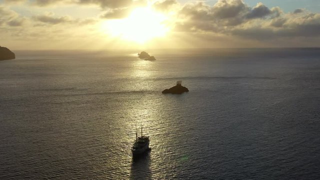 A tranquil sunset silhouettes rock islands and a pinisi schooner in Raja Ampat, Indonesia. This tropical region harbors amazing biodiversity and is a popular destination for divers and snorkelers.