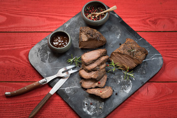 Sliced smoked roast beef with salt and pepper on marble plate on wooden old rustic table. Red background.