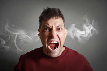 Portrait of angry man with steam coming out of ears on grey background