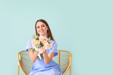 Beautiful young woman with bouquet of carnation flowers sitting in armchair on color background