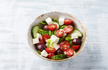 Salad with Kalamata Olives, Cucumber Cherry Tomatoes and Feta Cheese on bright wooden Background. Healthy Snack Idea. Close up.