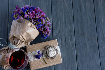 A glass of red wine close-up along with a bouquet of wildflowers and gift boxes on a dark wooden background. Birthday greeting card banner design.