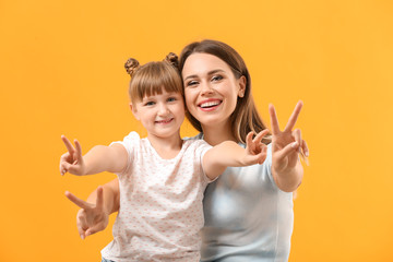 Portrait of happy mother and daughter showing victory gesture on color background