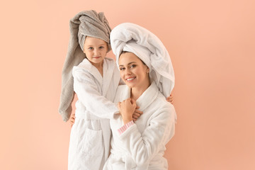 Portrait of happy mother and daughter in bathrobes on color background