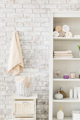 Fototapeta na wymiar Shelf unit with towels and cosmetics near brick wall in bathroom