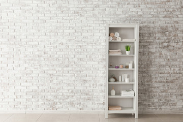 Shelf unit with towels and cosmetics near brick wall in bathroom
