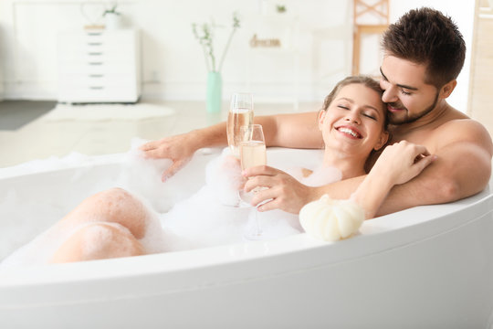 Happy young couple drinking champagne while taking bath together