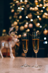 Two glasses of champagne standing on the blurred decorated christmas tree background.