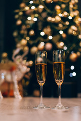 Two glasses of champagne standing on the blurred decorated christmas tree background.