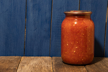 Baked homemade canned adjika on a blue background from boards on a wooden table.