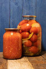 Baked homemade adjika pots and tomato on a blue background from boards on a wooden table.