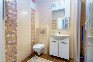 Fototapeta na wymiar Bathroom in the apartment. Shower, sink with mirror, toilet. Square ceramic tiles in the form of blue, yellow, red and white leaf patterns on the wall in the bathroom. White-yellow patterns alternate