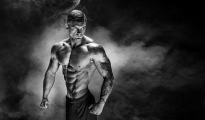 Fototapeta na wymiar Bodybuilder posing. Fitness tattooed muscled man on smoke background. Studio shot.