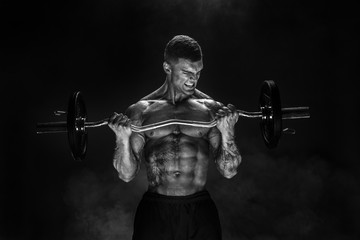 Studio portrait of topless bodybuilder performing biceps exercise with concentrated face over black...