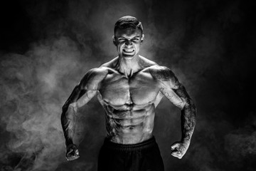 Fototapeta na wymiar Very brawny guy bodybuilder posing. Beautiful sporty guy male power. Fitness muscled man. Roar. Smoke background.