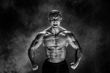 Fototapeta na wymiar Very brawny guy bodybuilder posing. Beautiful sporty guy male power. Fitness muscled man. Roar. Smoke background.